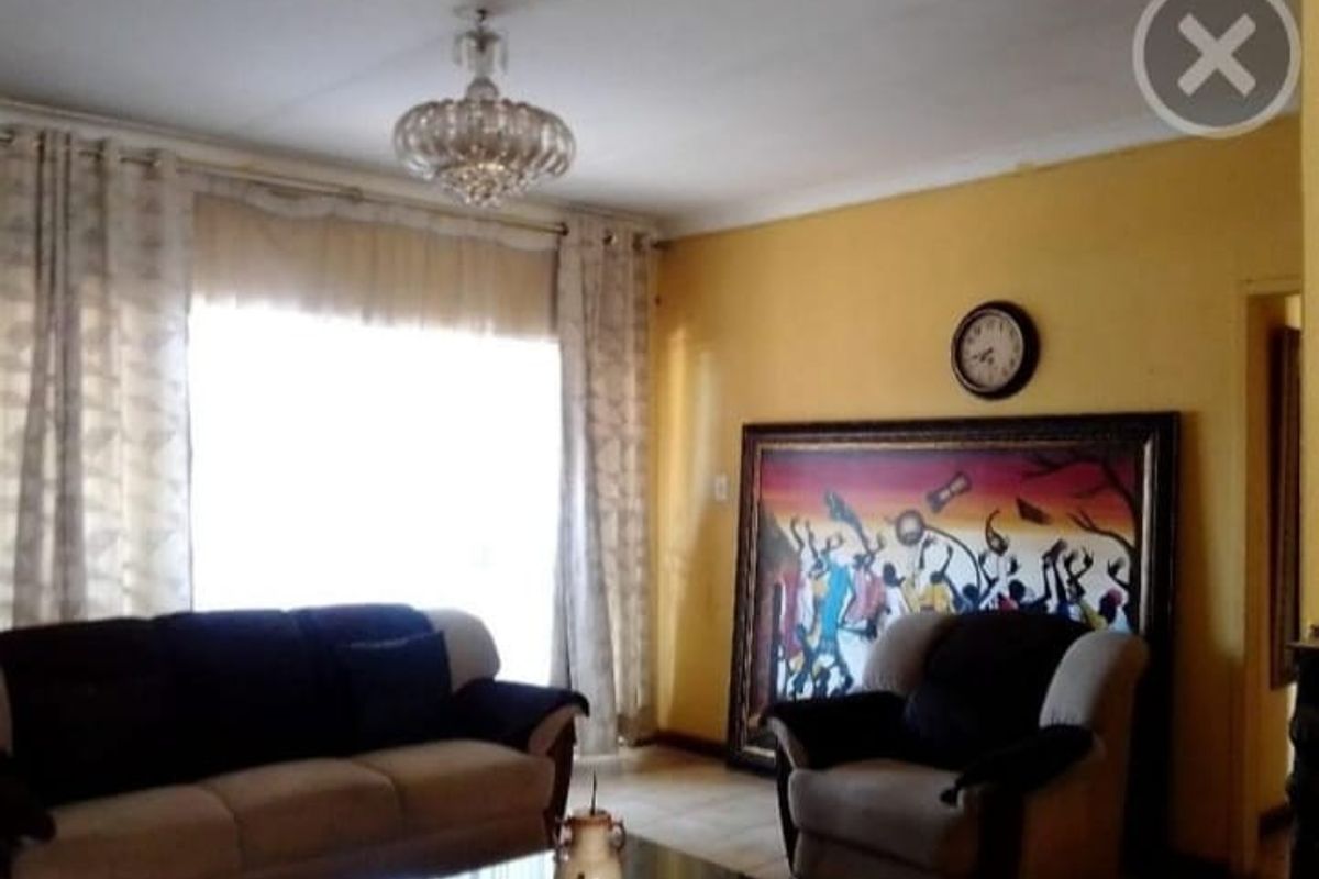 A living room featuring tiled flooring, a central chandelier, and large windows with curtains, providing a functional and comfortable living space.