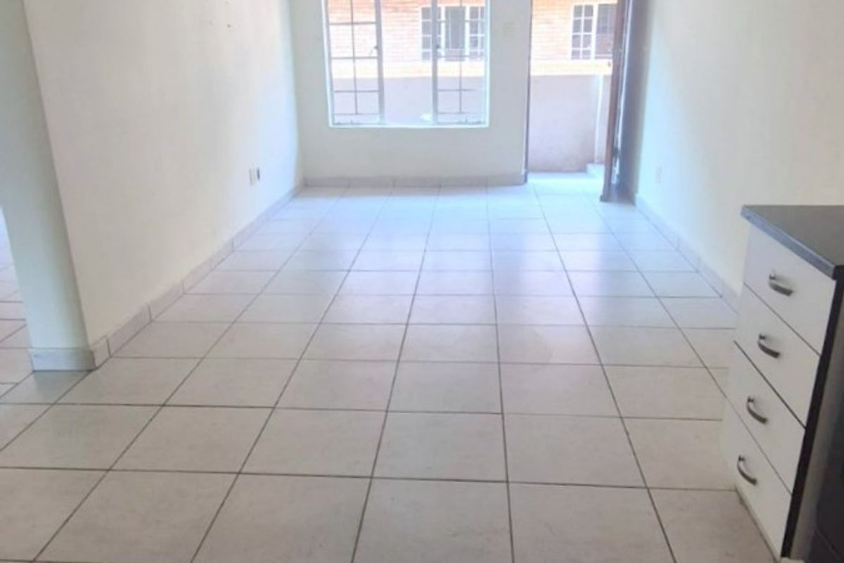 An empty, open-plan living area featuring neutral tiled flooring, natural light from a large window, and direct access to an outdoor space.