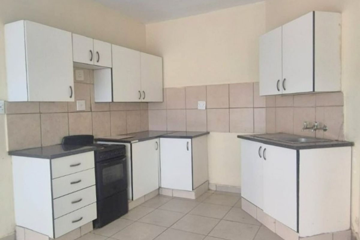 A functional kitchen featuring white built-in cabinetry, tiled backsplash, tiled flooring, and a freestanding stove, offering a clean and practical layout.