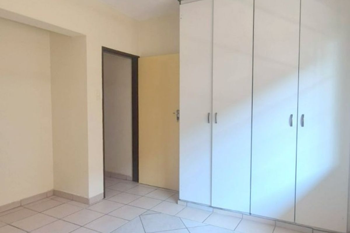 A clean, empty bedroom featuring neutral tiled flooring and white built-in cupboards, offering a blank canvas for personalization.