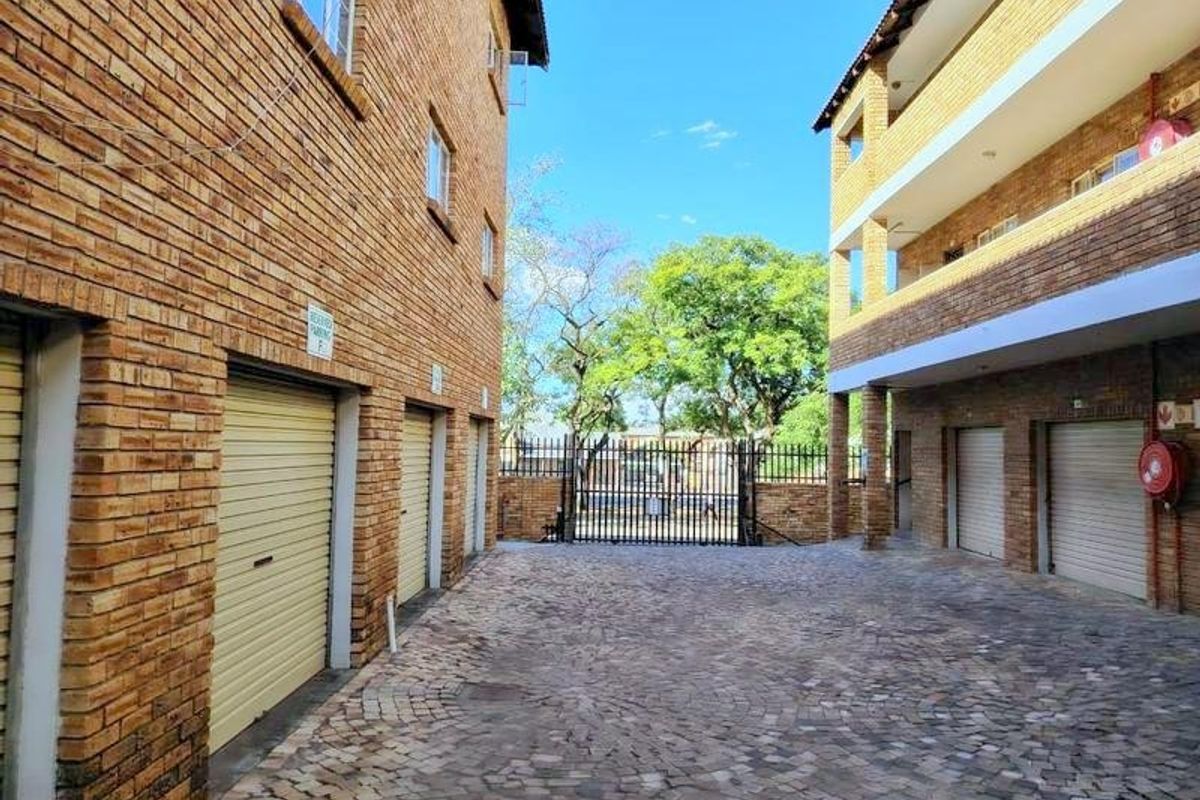 Exterior view of an apartment complex courtyard featuring brick facades, multiple roller shutter garage doors, and cobblestone paving.