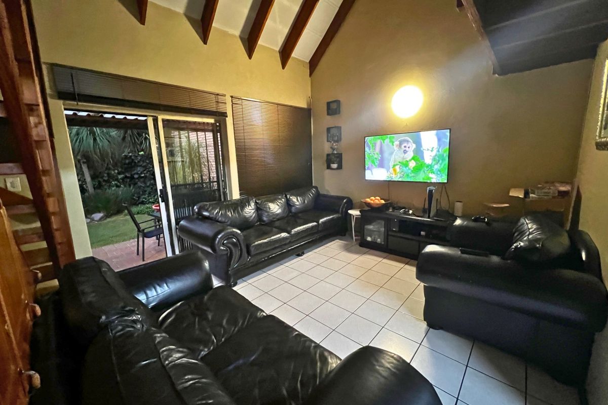 Spacious living room featuring high vaulted ceilings with exposed timber beams, tiled flooring, and sliding glass doors providing direct access to the rear garden.