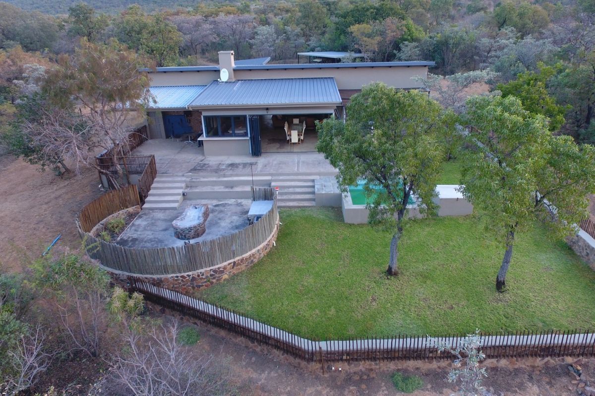 Aerial view of a modern residence featuring a swimming pool, tiered patio, built-in fire pit area, and landscaped garden set within a natural bushveld environment.