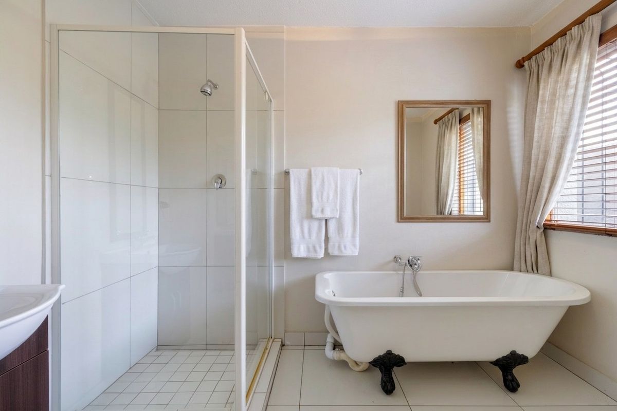 A bright bathroom featuring a classic clawfoot bathtub, a separate glass-enclosed shower, and neutral floor tiling.