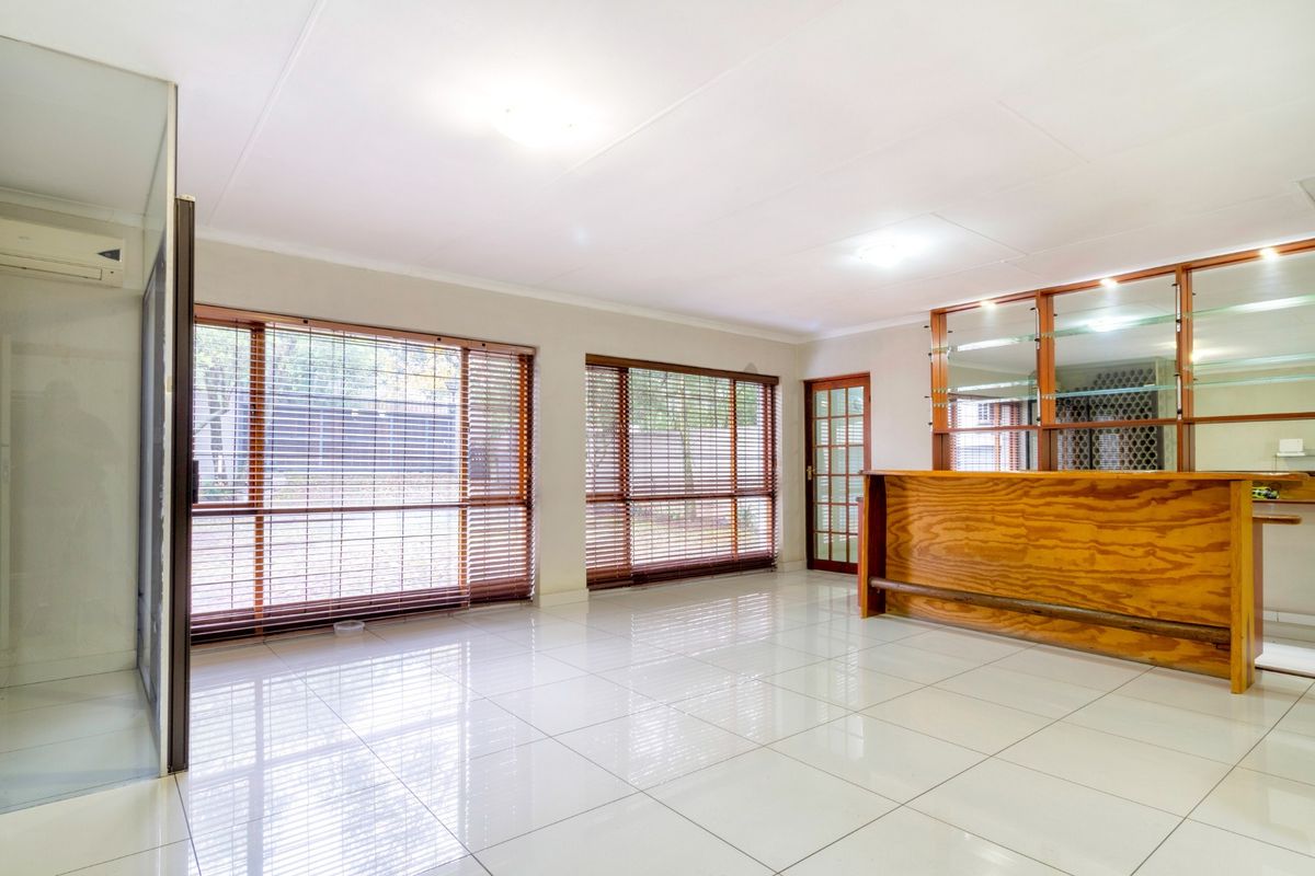 Spacious living area featuring polished floor tiles, large windows with wooden blinds, and a built-in wooden bar with glass shelving.