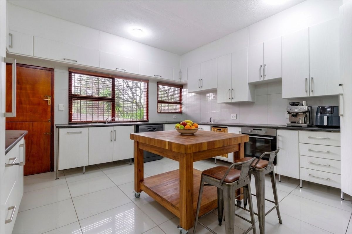 A bright, functional kitchen featuring white cabinetry, dark countertops, tiled flooring, and a central wooden island, providing ample workspace and storage.