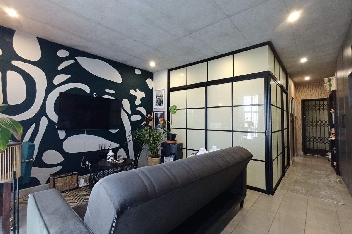 Modern living area featuring a striking patterned feature wall, industrial-style glass partition, and tiled flooring, creating a contemporary and well-defined open-plan space.