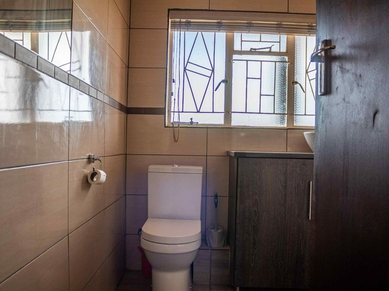 A compact bathroom featuring floor-to-ceiling wall tiles, a modern toilet, and a built-in vanity cabinet with a window providing natural light.