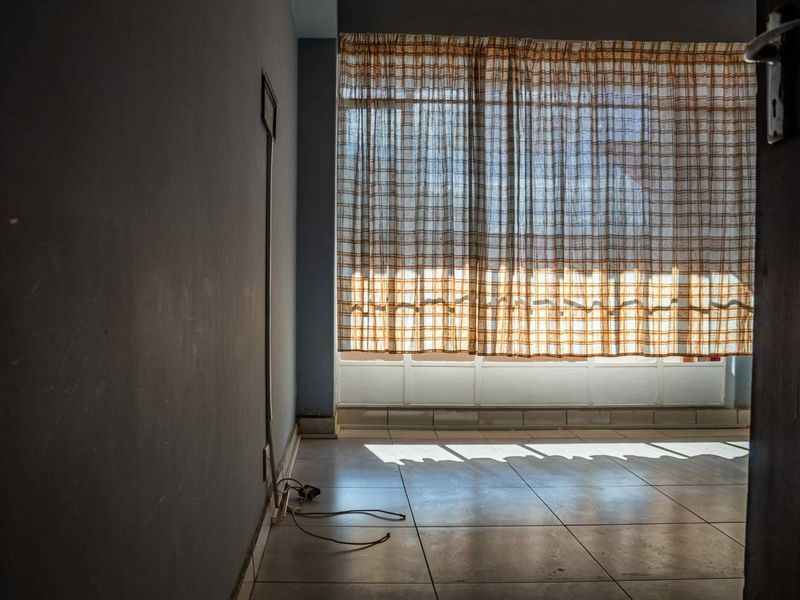 An empty room featuring tiled flooring and a large window with curtains, showing signs of wear and requiring cosmetic updates.