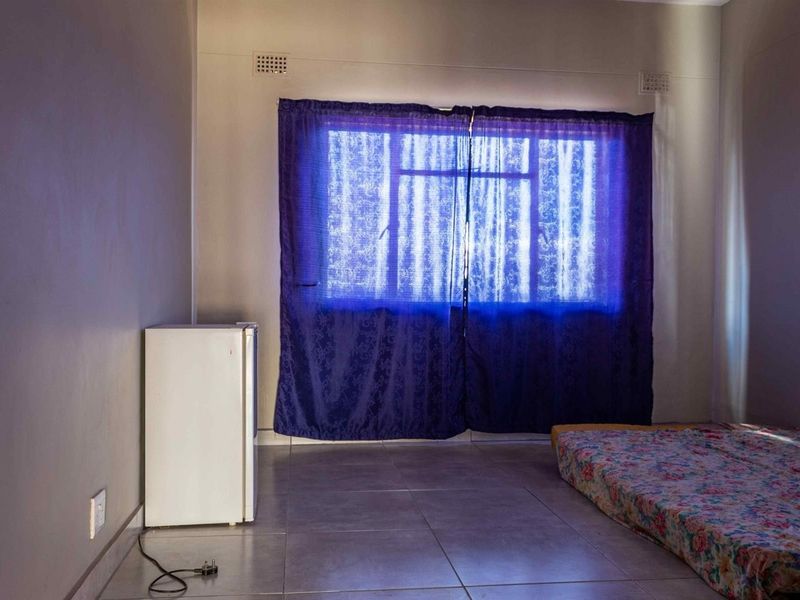 A simple bedroom featuring tiled flooring, a window with curtains, and built-in ventilation vents.