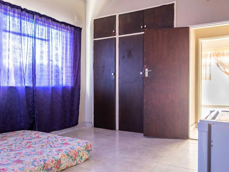 A bedroom featuring built-in wooden cupboards and tiled flooring, offering a functional space with potential for modernization.