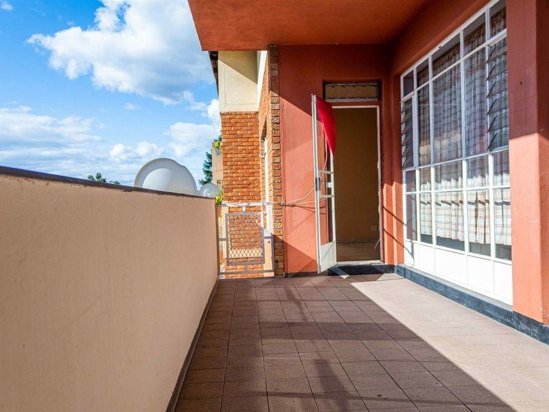 A covered balcony featuring tiled flooring, brick accents, and large glass windows, providing an outdoor space accessible from the interior.