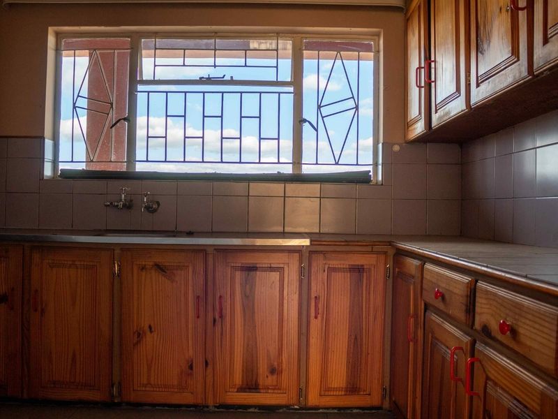 A dated kitchen featuring wooden cabinetry, tiled splashbacks, and a stainless steel sink with a window view.