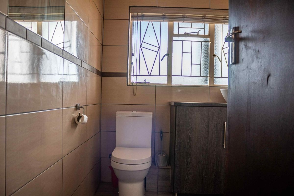A compact bathroom featuring floor-to-ceiling wall tiles, a modern toilet, and a built-in vanity cabinet with a window providing natural light.