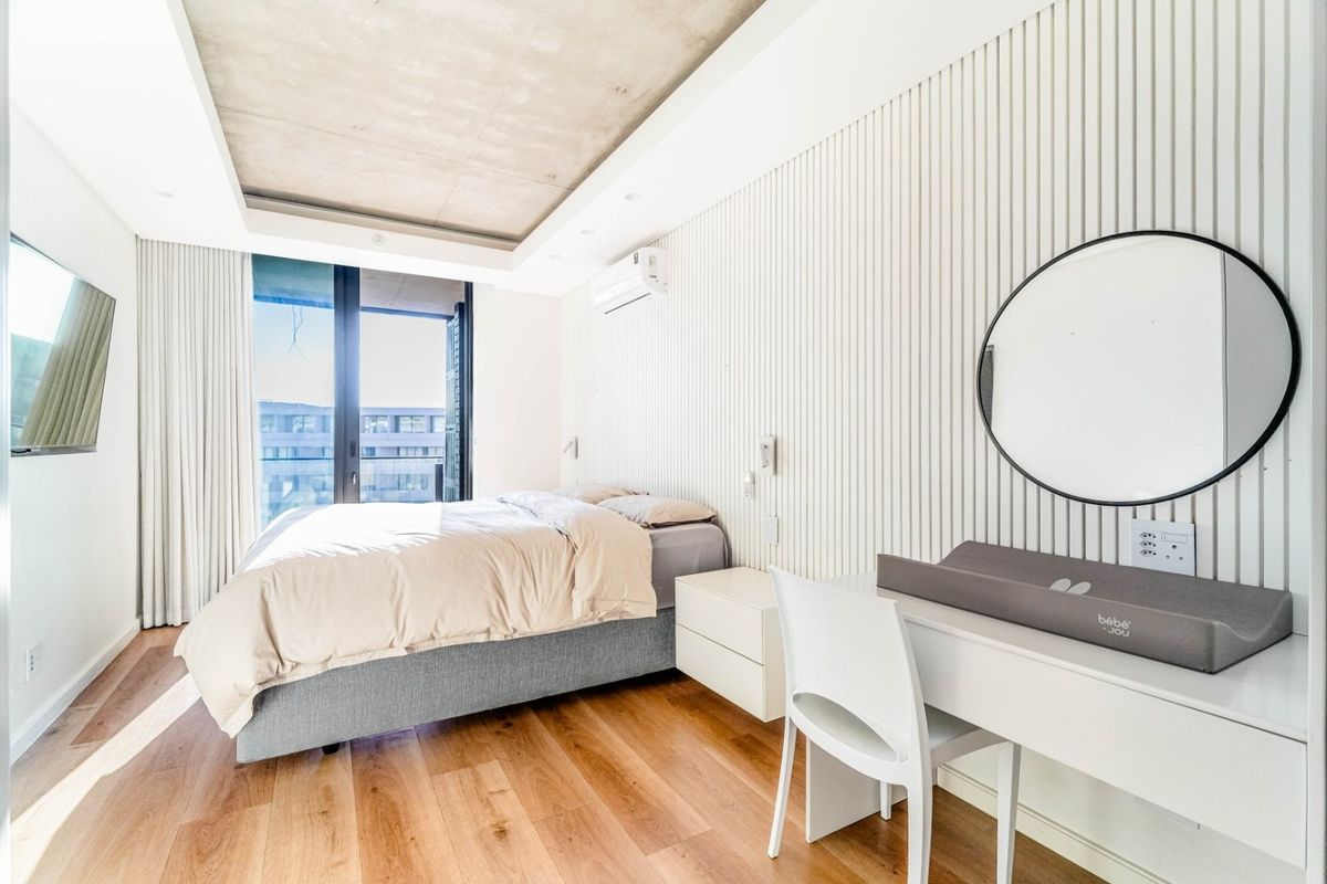 Modern bedroom featuring a raw concrete ceiling, timber flooring, vertical slat wall paneling, and a sliding glass door leading to a balcony.