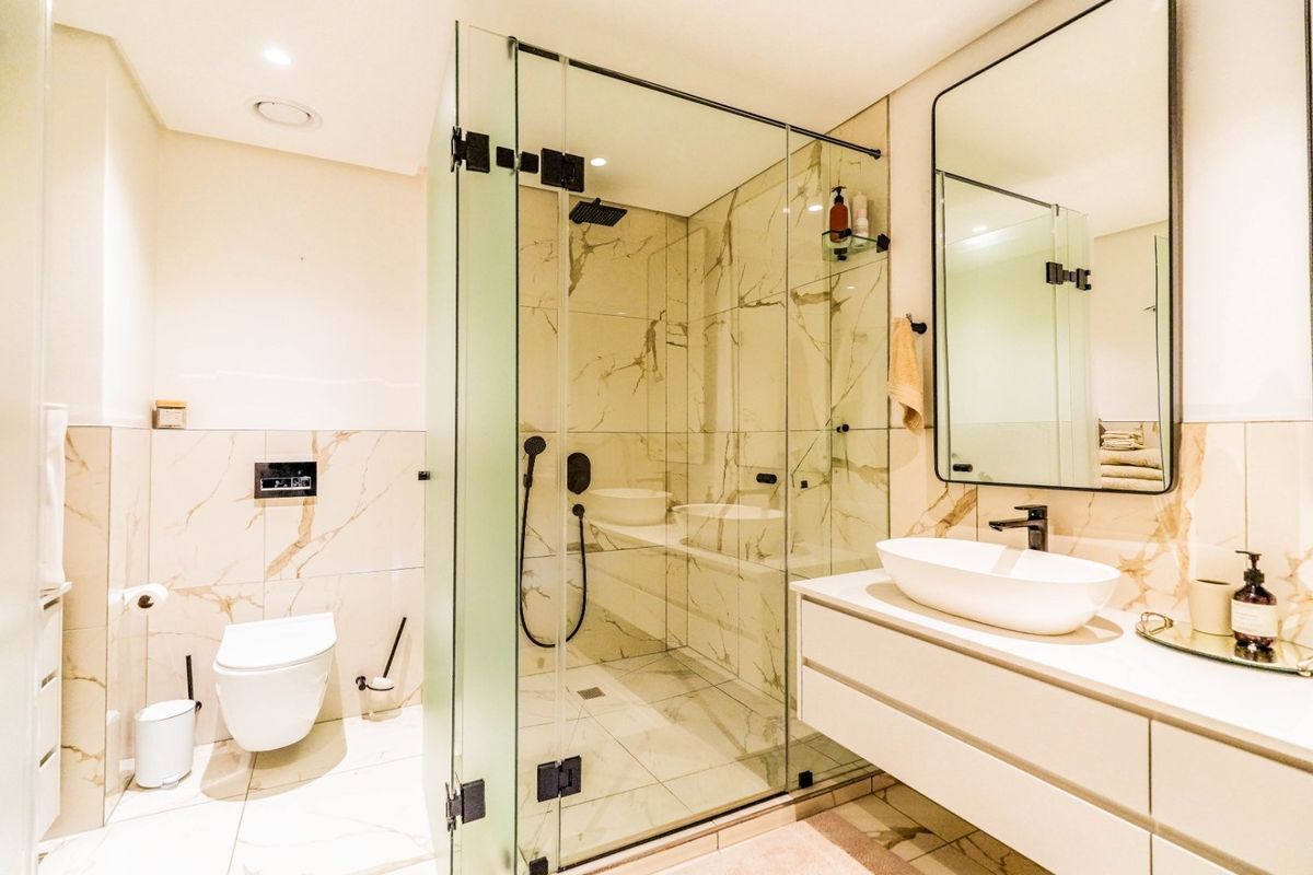 Modern bathroom featuring a walk-in glass shower, wall-mounted toilet, and a sleek vanity with a vessel sink and marble-look tiling.