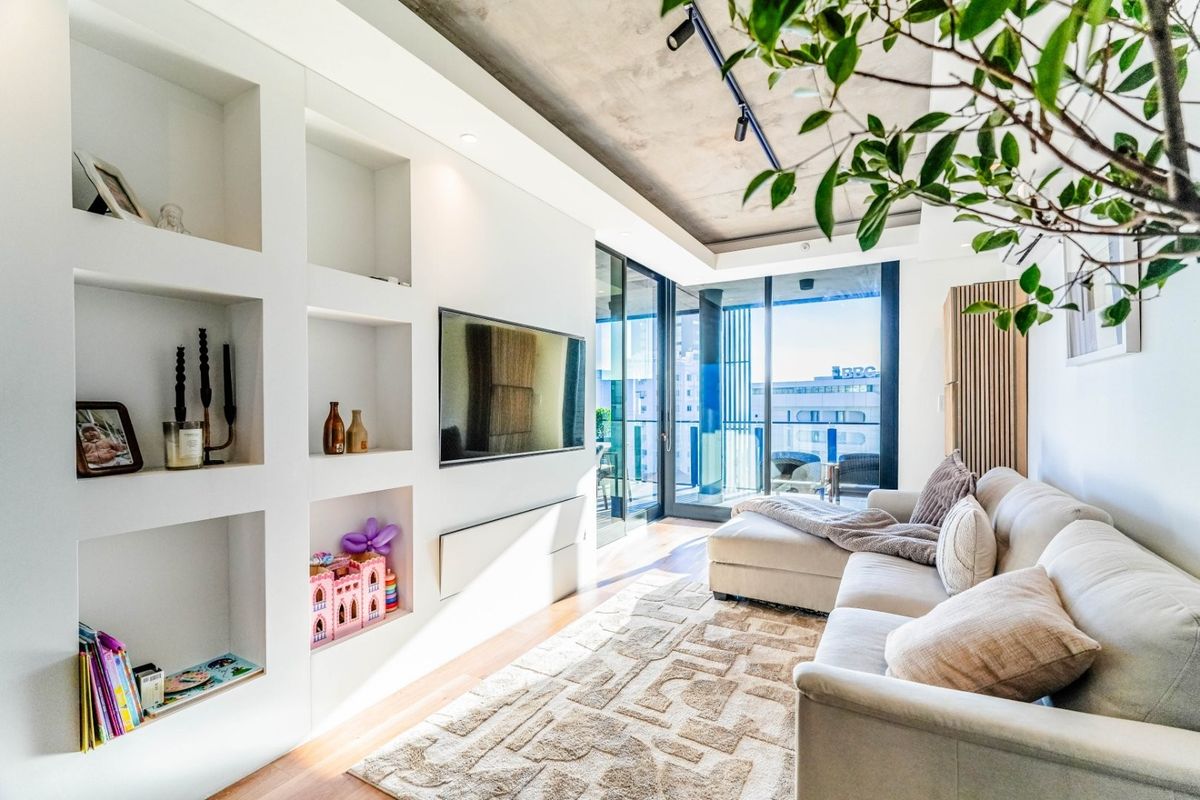 Modern living room featuring built-in shelving, exposed concrete ceiling, track lighting, and large sliding glass doors leading to a private balcony.