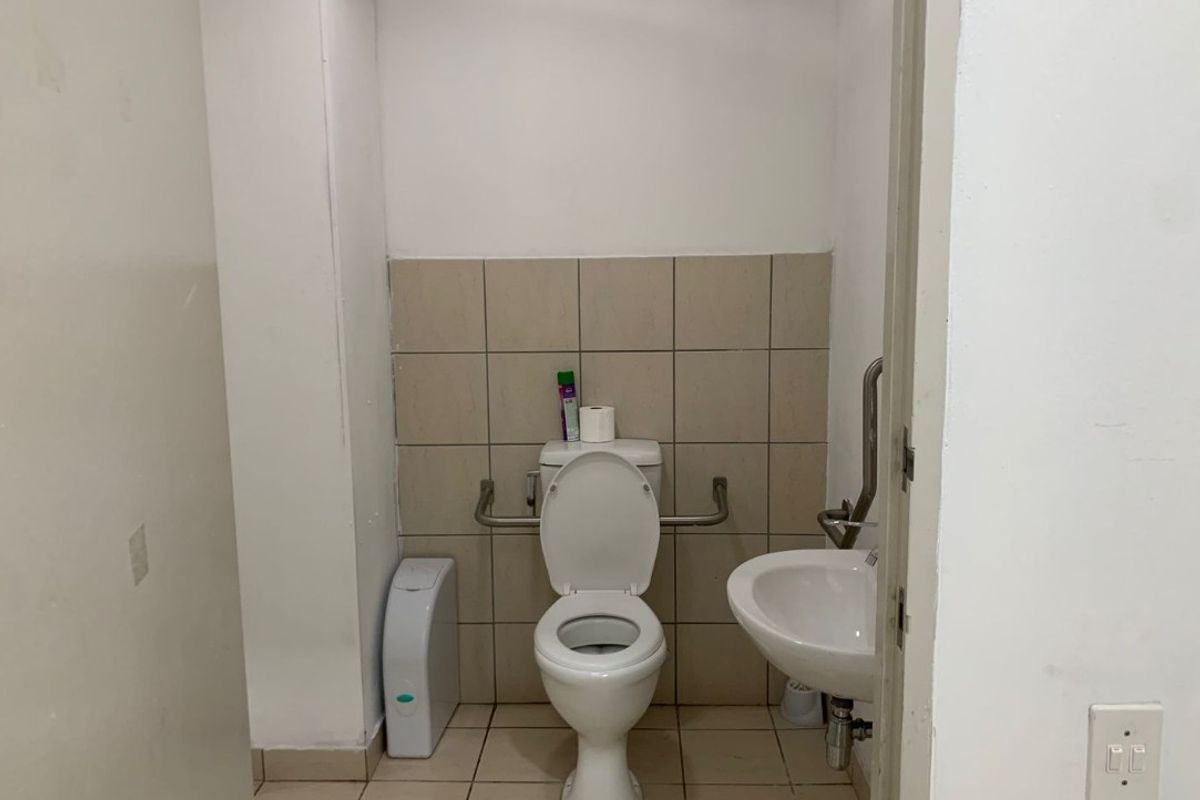 A functional accessible restroom featuring a toilet, wall-mounted basin, and safety grab rails with tiled flooring and splashback.