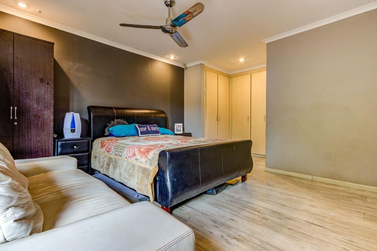 Spacious bedroom featuring built-in wooden cupboards, laminate flooring, and a ceiling fan, offering a functional layout with neutral wall tones.