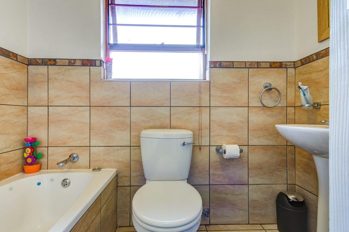 A functional bathroom featuring a built-in bathtub, pedestal basin, and toilet with neutral wall tiling and a window for natural light.