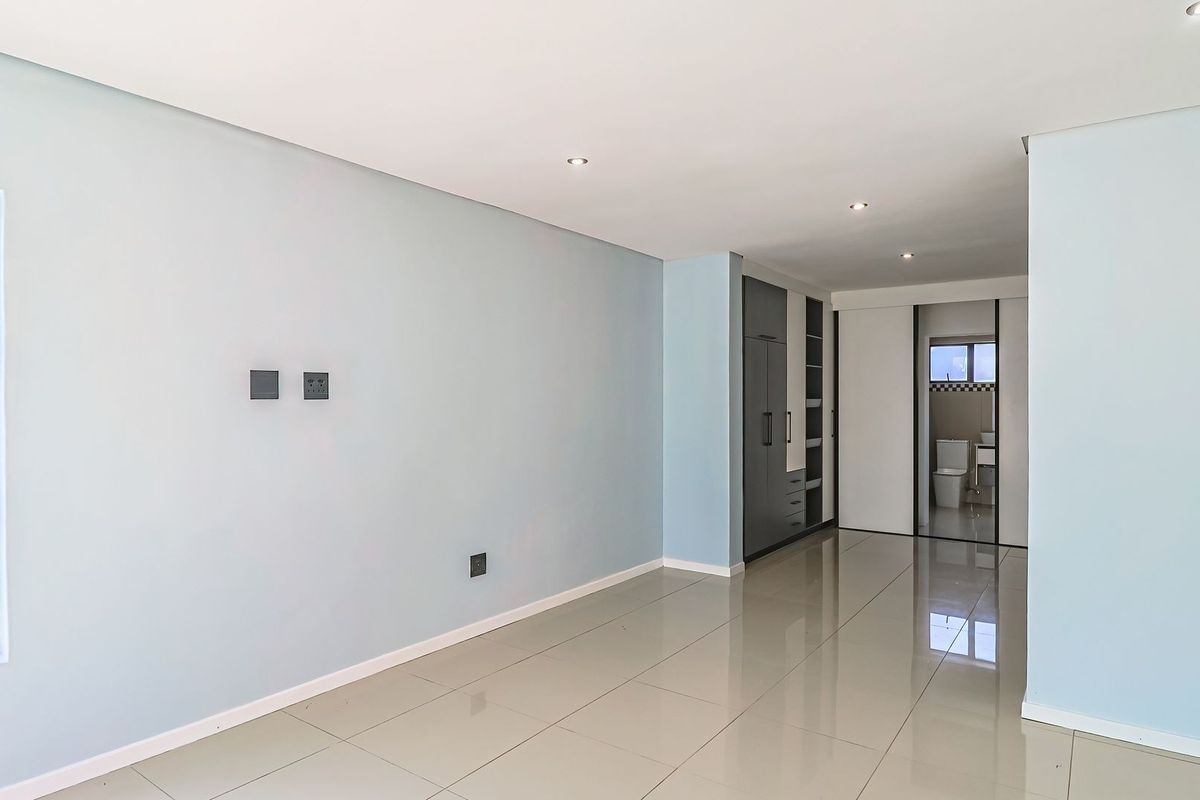 A bright, empty bedroom featuring modern tiled flooring, built-in cupboards, and recessed downlighting, with an adjoining en-suite bathroom visible.