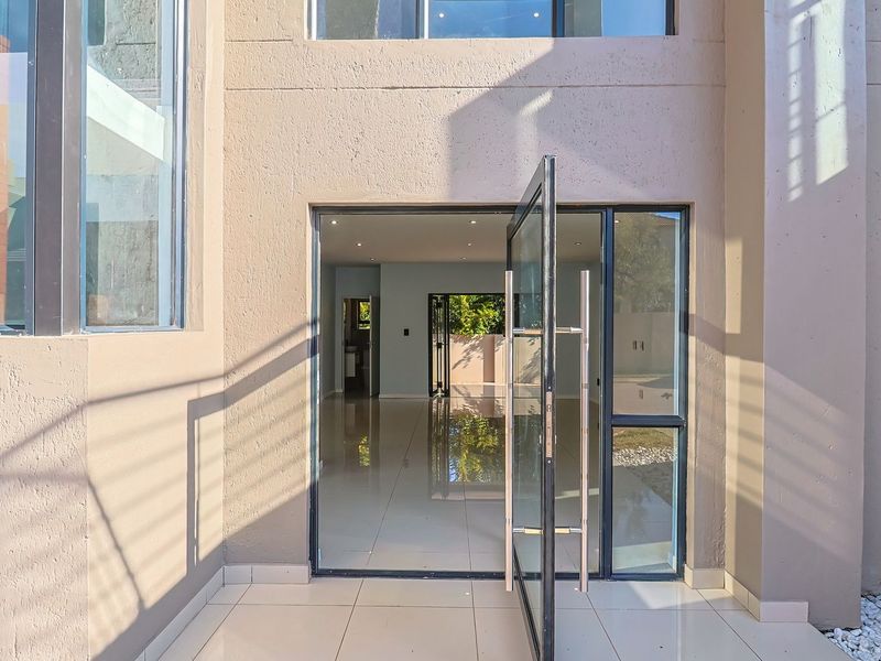Modern entrance featuring a large glass pivot door, tiled flooring, and double volume architectural design, providing a bright and welcoming transition into the home.