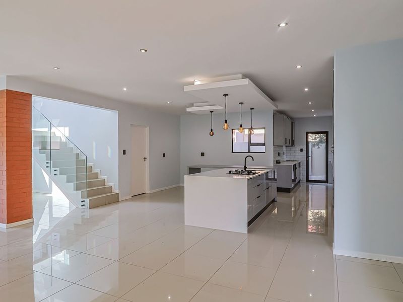 Spacious open-plan living and kitchen area featuring a modern island with gas cooktop, sleek cabinetry, and a striking exposed brick staircase feature.