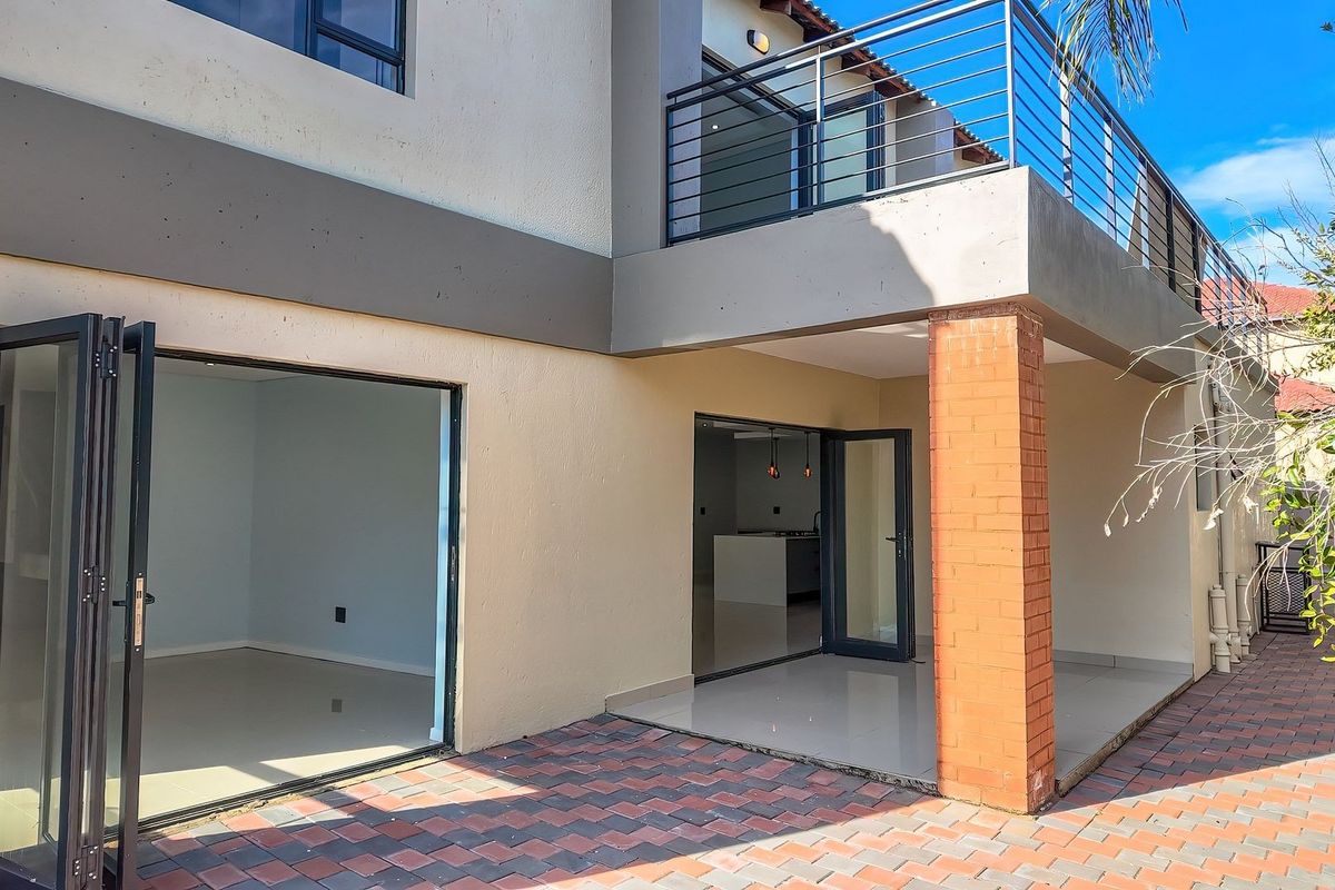 Rear exterior view featuring a paved patio area, bi-fold doors leading to the interior, and an upper-level balcony with metal railings.