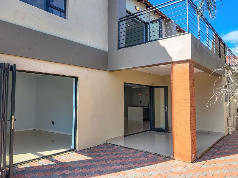 Rear exterior view featuring a paved patio area, bi-fold doors leading to the interior, and an upper-level balcony with metal railings.