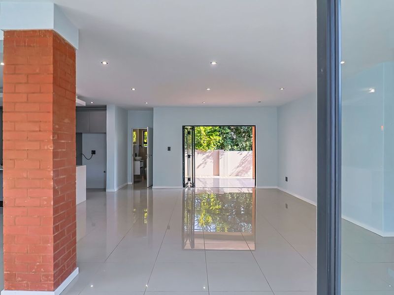 Spacious open-plan living area featuring polished porcelain tiles, a striking exposed brick pillar, recessed lighting, and seamless access to the outdoor patio.