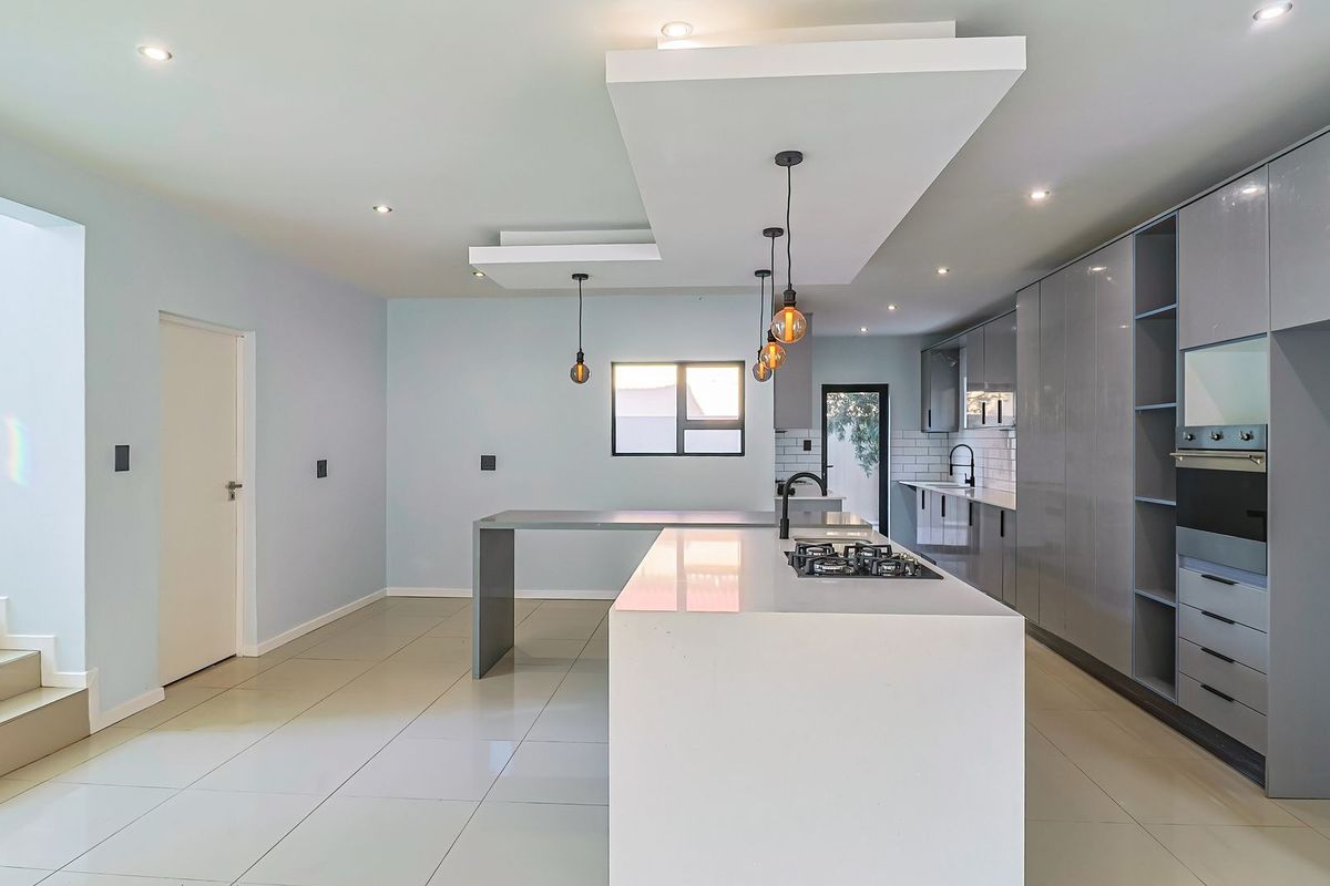 Modern, spacious kitchen featuring a large central island, sleek grey cabinetry, built-in oven, gas hob, and contemporary recessed and pendant lighting.