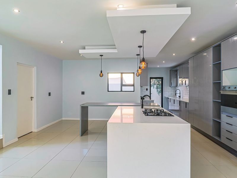 Modern, spacious kitchen featuring a large central island, sleek grey cabinetry, built-in oven, gas hob, and contemporary recessed and pendant lighting.