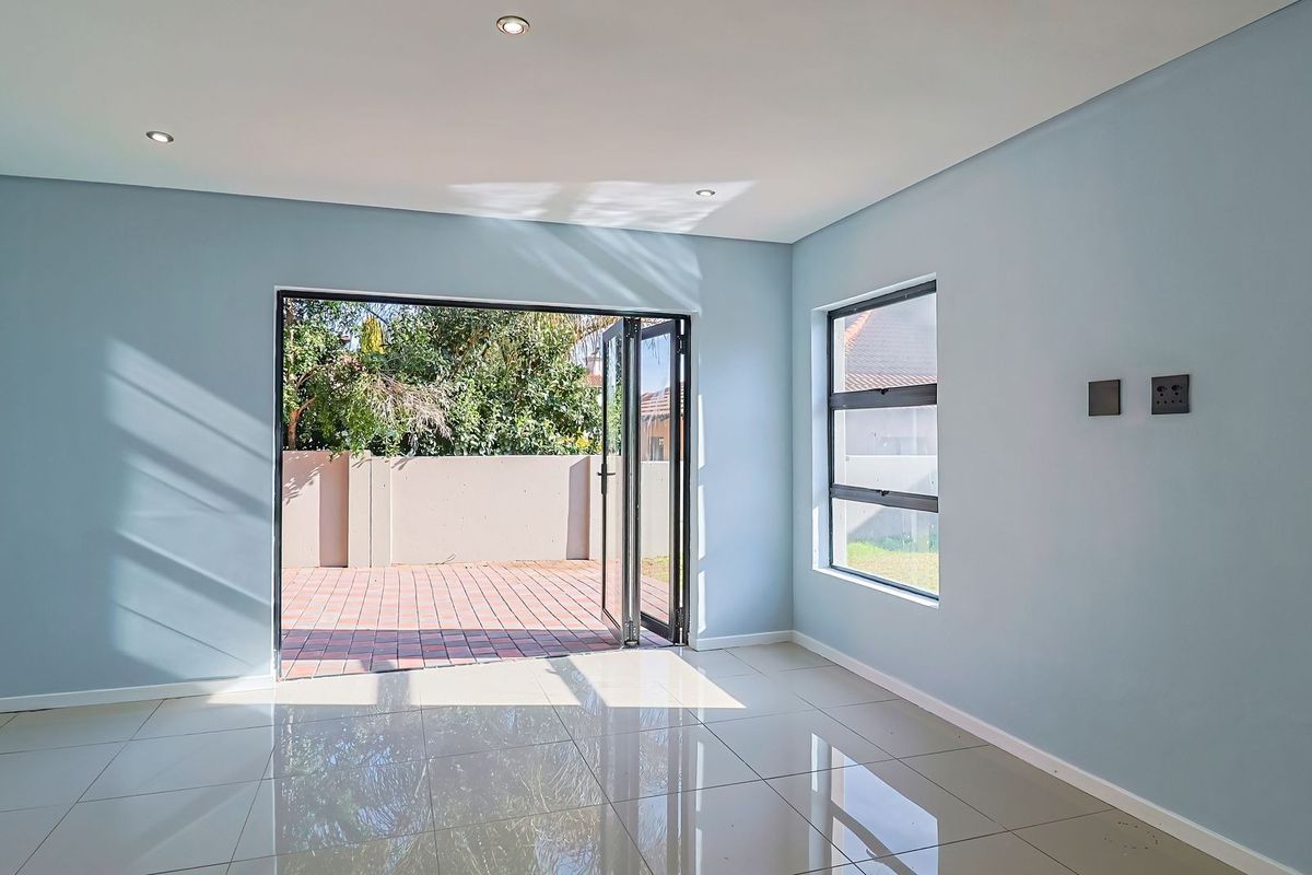 A bright, empty living room featuring tiled floors, recessed lighting, and large aluminium stacker doors opening onto a paved patio area.