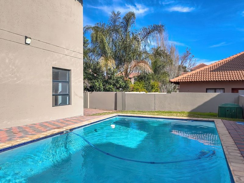 A well-maintained outdoor swimming pool area featuring paved surrounds and a secure boundary wall, set against the side elevation of the house.