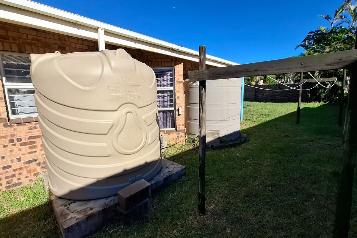Rear exterior view featuring two large plastic water storage tanks positioned against the brick house wall, alongside a wooden washing line structure.