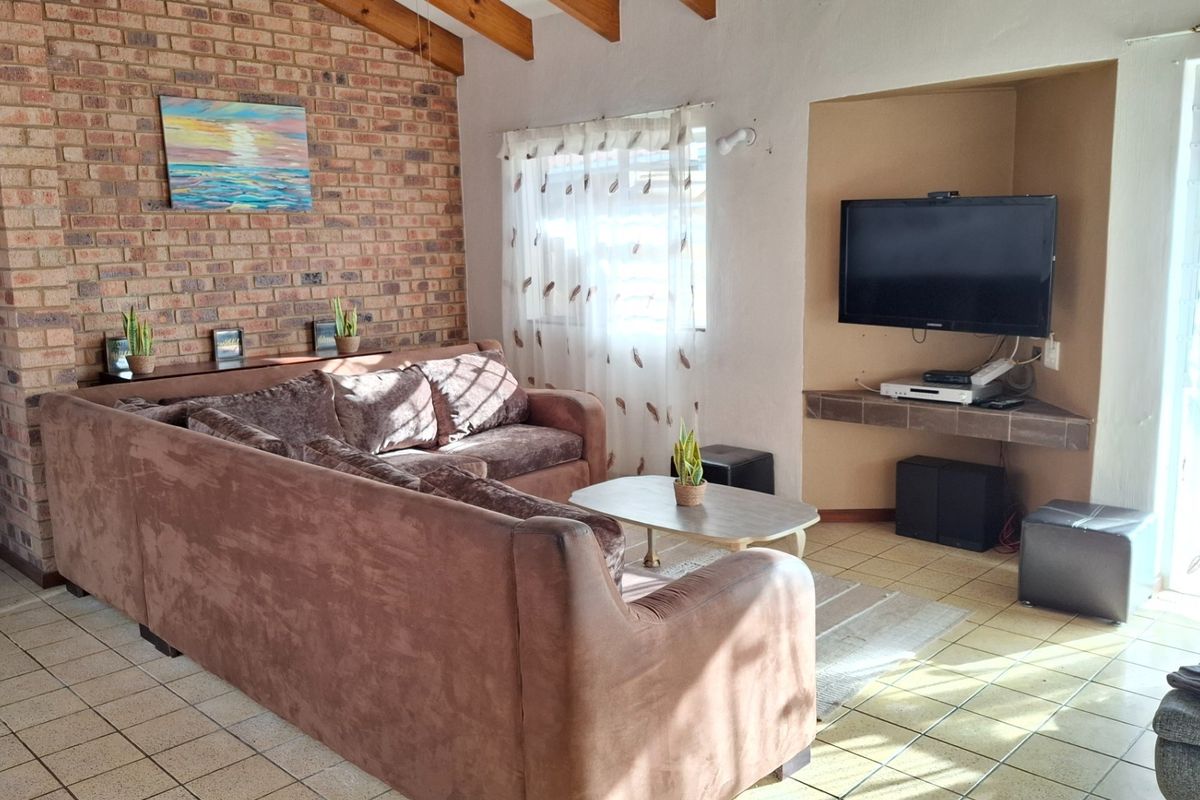 A living room featuring exposed brick walls, vaulted timber ceilings, and tiled flooring with a built-in corner television alcove.