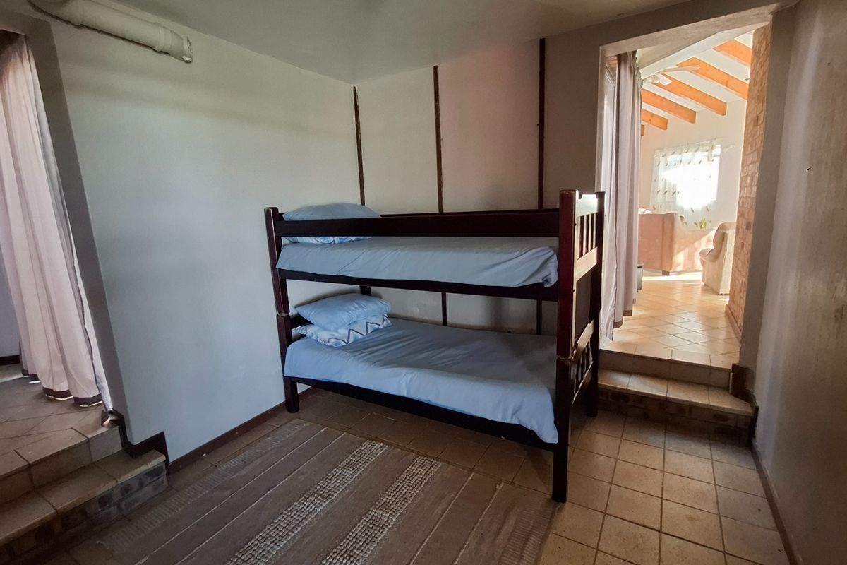A bedroom featuring tiled flooring and a step-up transition to an adjacent living area with exposed timber ceiling beams.
