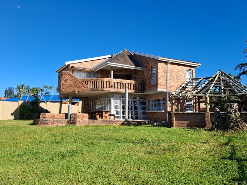 Rear view of a double-story face-brick house featuring a balcony, patio area, and a timber pergola structure set within a spacious garden.