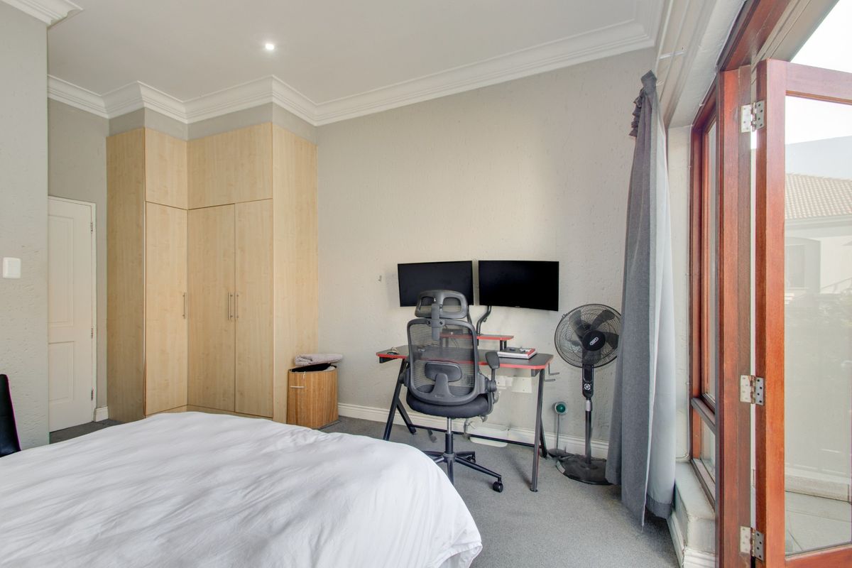 A well-lit bedroom featuring built-in wooden cupboards, neutral wall finishes, and direct access to an outdoor area through wooden-framed doors.