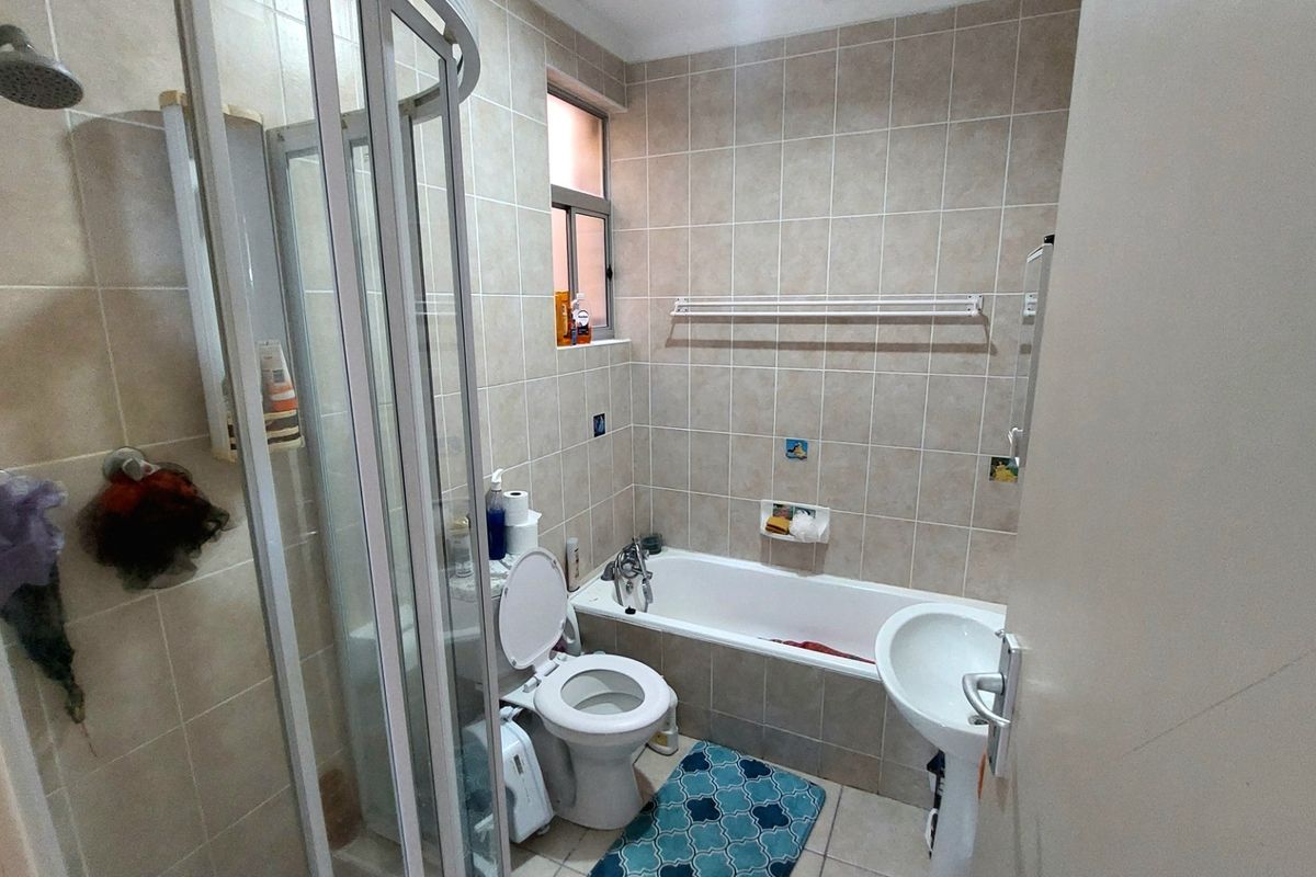 A functional bathroom featuring a separate shower enclosure, a standard bathtub, a pedestal sink, and neutral wall tiling.