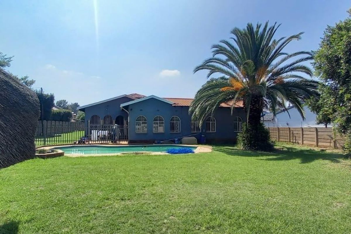 Rear view of the property featuring a swimming pool, landscaped garden, and a thatched lapa structure.