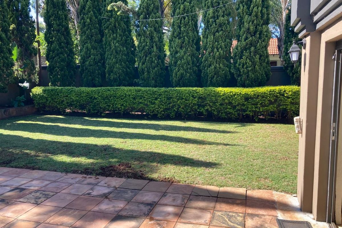 A private rear garden featuring a paved patio area, well-maintained lawn, and established hedge and tree screening for privacy.