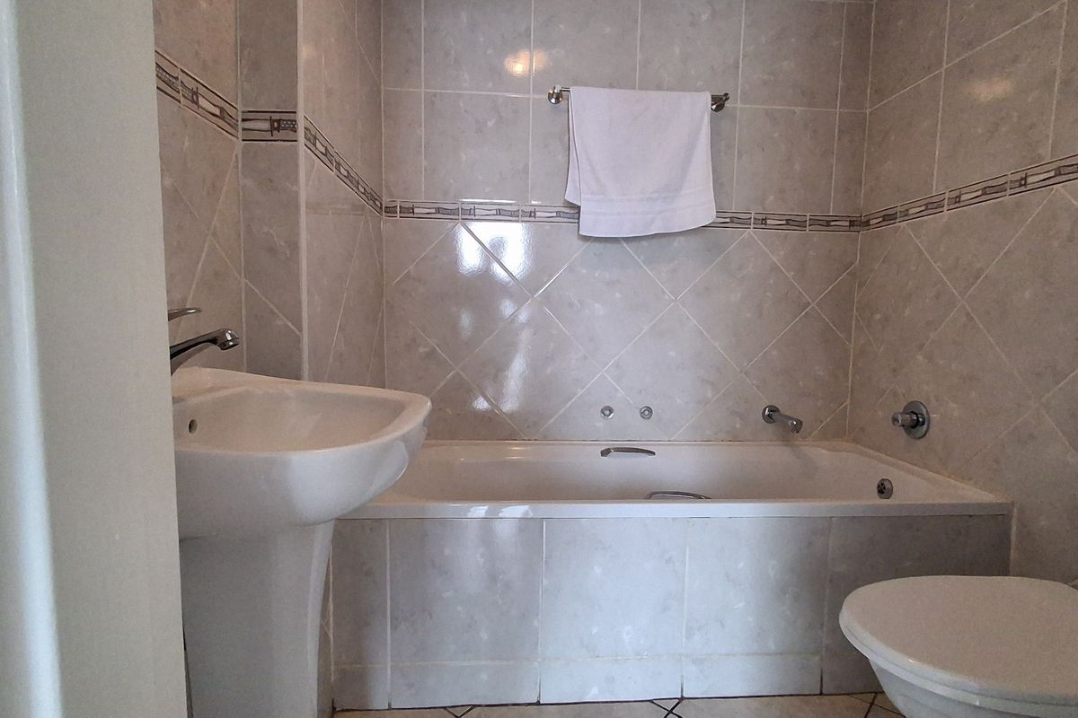 A functional bathroom featuring a pedestal basin, a built-in bathtub with wall-mounted fixtures, and a standard toilet, finished with neutral wall tiles.
