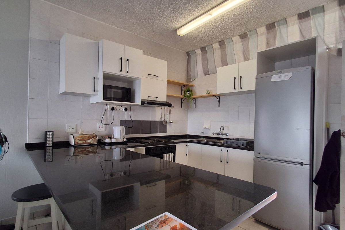 A functional kitchen featuring dark granite countertops, white cabinetry, a built-in hob, and a double sink with tiled splashbacks.