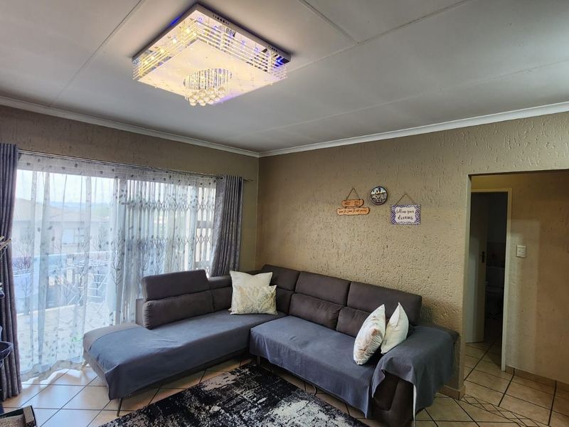 A living room featuring tiled flooring, a decorative crystal ceiling light fixture, and large sliding glass doors with security gates.