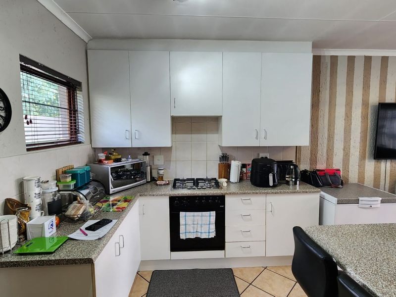 Functional kitchen featuring white cabinetry, granite-look countertops, built-in gas hob, and oven, integrated into an open-plan living space.