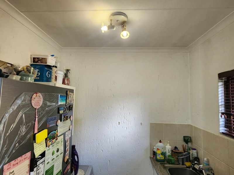 A functional scullery area featuring a stainless steel sink, tiled splashback, and window with blinds, providing a practical space for kitchen preparation and cleaning.