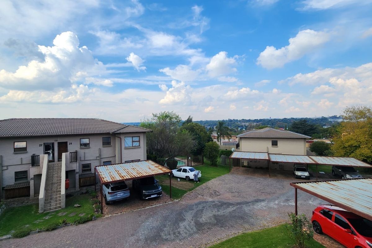 Elevated view of the apartment complex grounds, featuring paved parking areas, covered carports, and surrounding landscaped garden space.