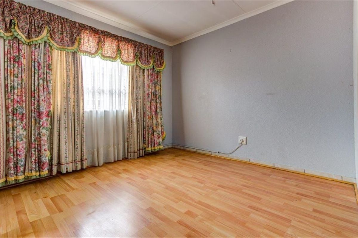 A bedroom featuring laminate wood flooring, neutral wall paint, and a window with decorative pelmet and curtains.
