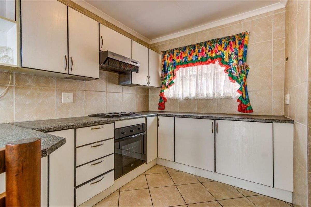 A functional kitchen featuring built-in cabinetry, a fitted oven, a gas hob, and an extractor fan, finished with tiled walls and flooring.